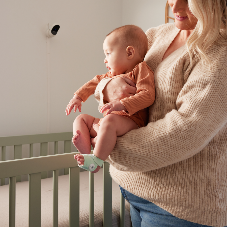 Moeder met baby bij de wieg, met de Owlet-camera aan de muur